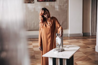 Photo of a woman pushing down on the lever of a soda maker, carbonating an attached bottle of water