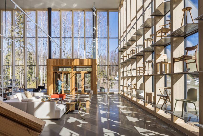 Photo of the entrance interior to the Finnish Design Shop hub with light pouring through glass curtain walls and chairs displayed in shelves that reach high up the glazing