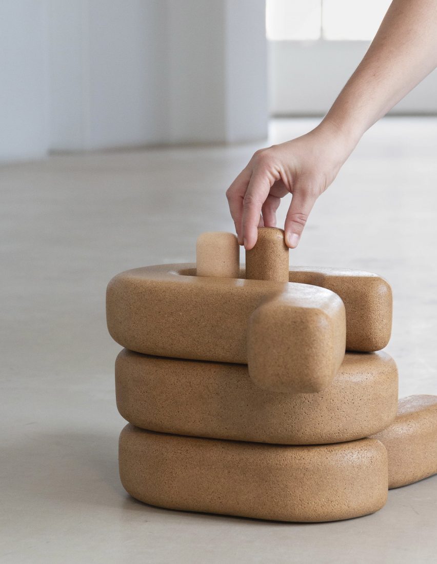 A hand assembles several pieces of brown, cork-like furniture