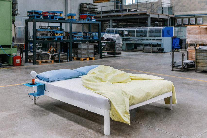 Photograph of a white bed with yellow and blue bed sheets in an industrial factory