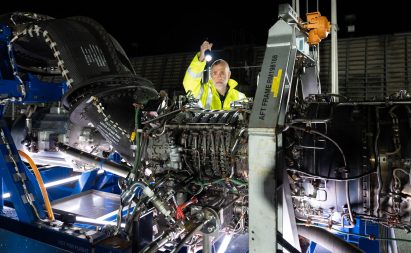 Photo of a man in hi-vis shining a light into the parts of a large aircraft engine