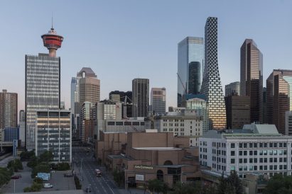 The skyline of Calgary, Alberta, featuring a new curvaceous tower by BIG. The sky is cloudless and it is nearing sunset, reflected in the buildings.