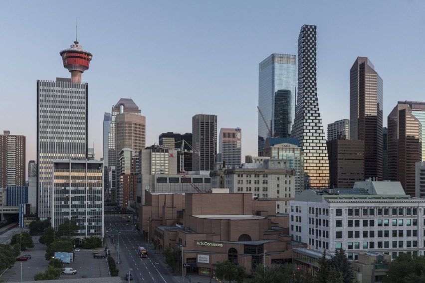 The skyline of Calgary, Alberta, featuring a new curvaceous tower by BIG. The sky is cloudless and it is nearing sunset, reflected in the buildings.
