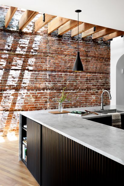 Light shines down past exposed floor joists onto an original brick wall
