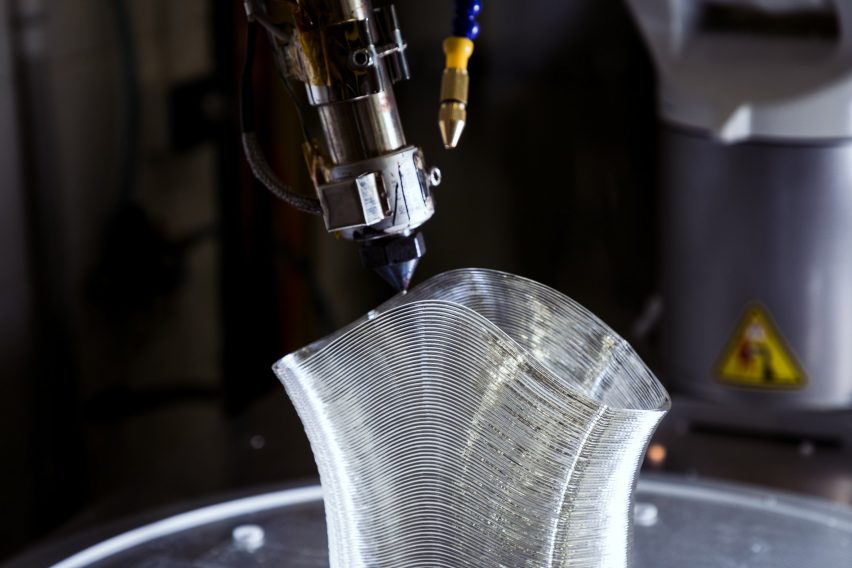 Photo of a 3D printer nozzle extruding clear plastic in a layers to form a tube
