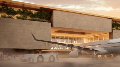 Airplane parked at a terminal clad in beige stone with greenery
