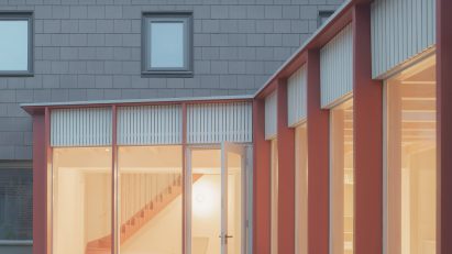 Grey house facade with red timber extension