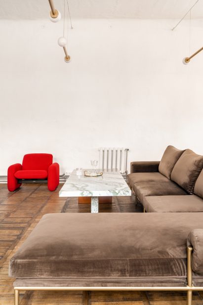 Photograph showing lounge area with brown-grey velvet sofa and red rounded armchair