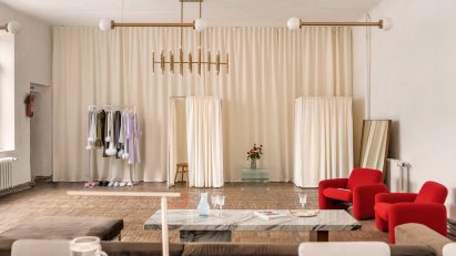 Photograph showing lounge area with brown-grey velvet sofa and red rounded armchairs