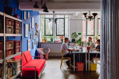 Picture of a workspace with a communal desk in the centre, plants and green large windows in the background