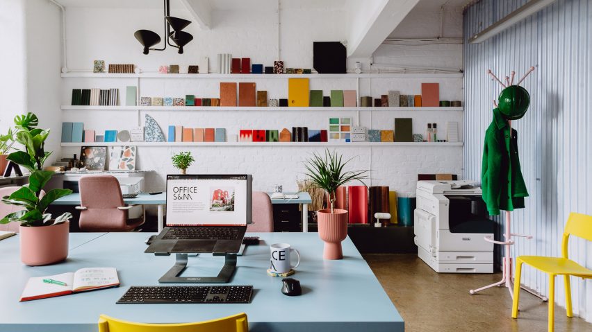 Picture of an office with a wall of different material samples and a blue desk in the centre of the space