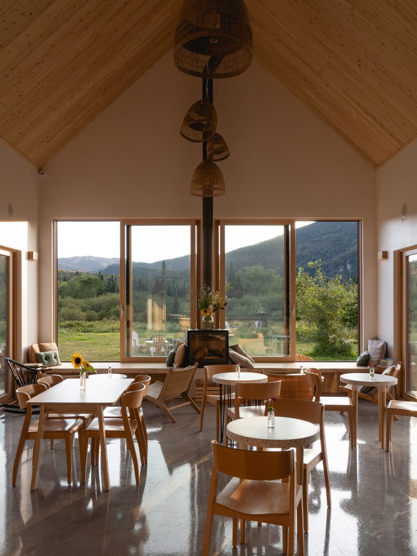 Cafe interior with wooden furniture and large windows overlooking a grassy hill
