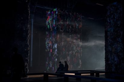 Two people sitting in front of a tower of clothes