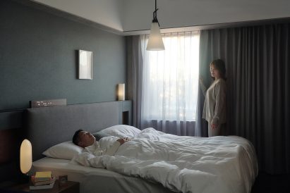 Photo of a person drawing a curtain in a darkened bedroom to let the morning light in