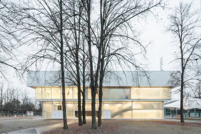 Photograph of low-slung white building with glazing with tree in foreground