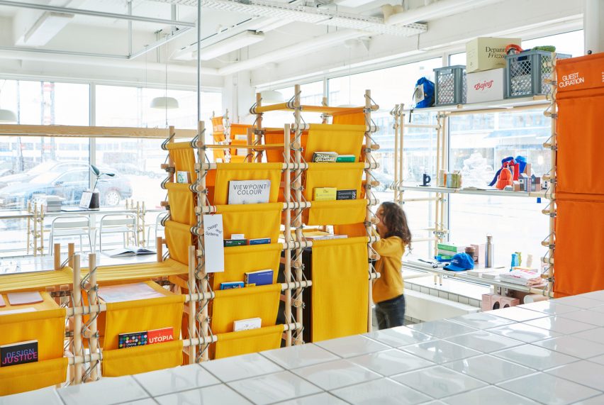 Photo of a child grabbing a book from the bright yellow fabric shelving of Space10's library, with shelves holding design objects in the background