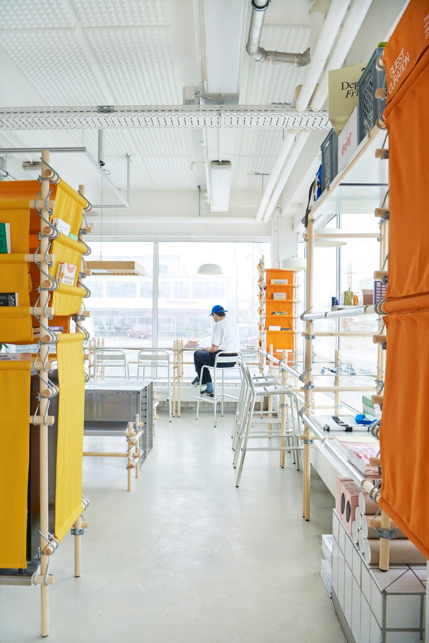 Photo of a person in a baseball cap sitting and reading at metal bar seating at the window of Space10's community space