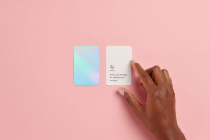 A hand fingers a small card with text that reads "could your feelings be affecting your thought?"