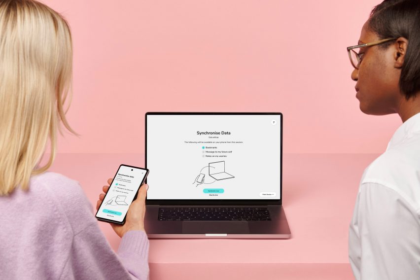 Two women look at a laptop and phone screen that display options for sychronising data
