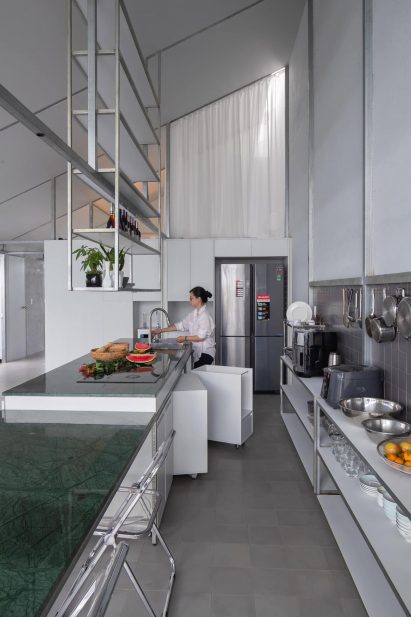Mono-pitched steel kitchen with green marble table and overhead shelving