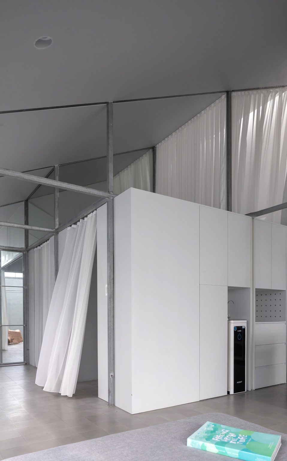 Mono-pitched steel interior with a white box room and white curtains