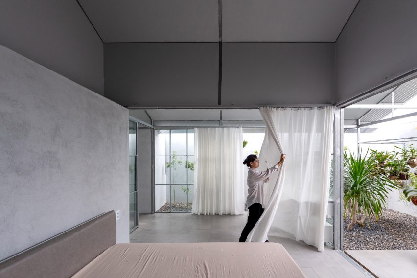 A grey bedroom with a white curtain room divider being pulled back