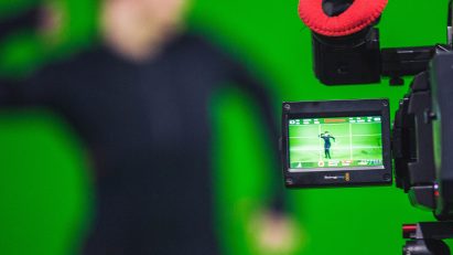 Photo of a camera filming an actor wearing a motion capture suit against a green screen