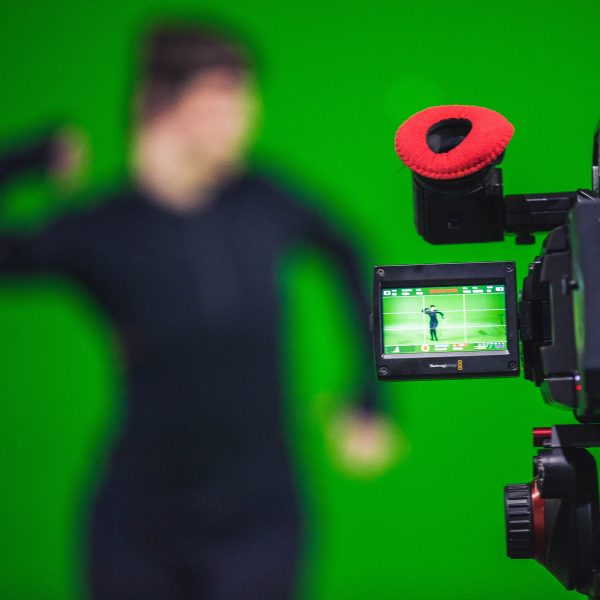 Photo of a camera filming an actor wearing a motion capture suit against a green screen