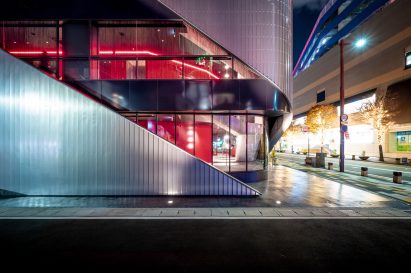 Exterior of the ground floor of a theatre building with glazed walls partly covered by slanted steel panels