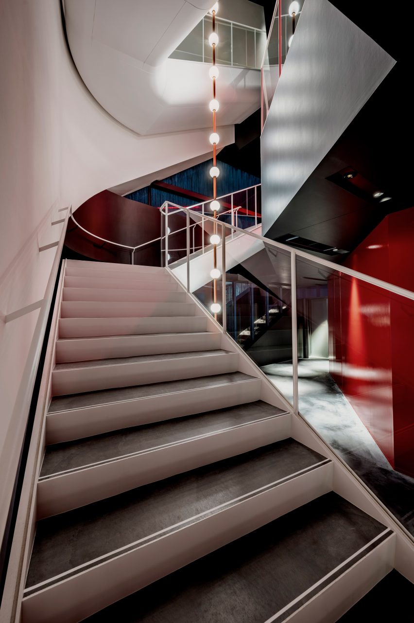 Staircase in an atrium space with suspended lighting at the centre and white and red walls