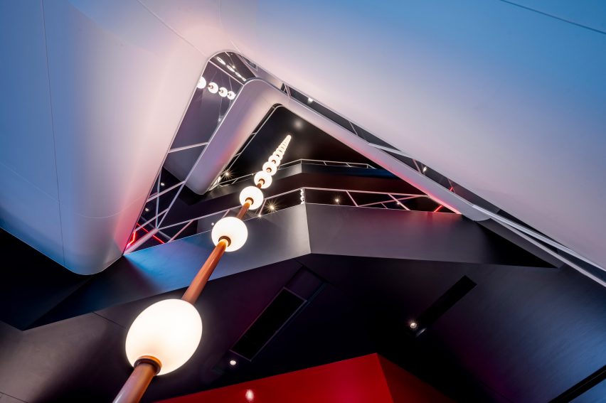 Triangular atrium in a cultural building with white walls, dark grey floor levels and suspended lighting