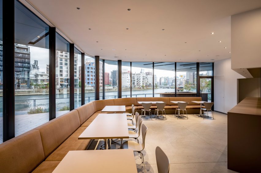 Restaurant interior with bench seating along a wall with large windows overlooking a terrace and waterfront