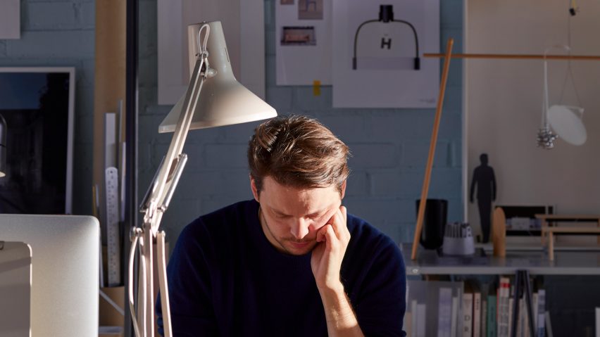 Daniel Rybakken sits at a desk in his studio, with drawings pinned to the wall behind him