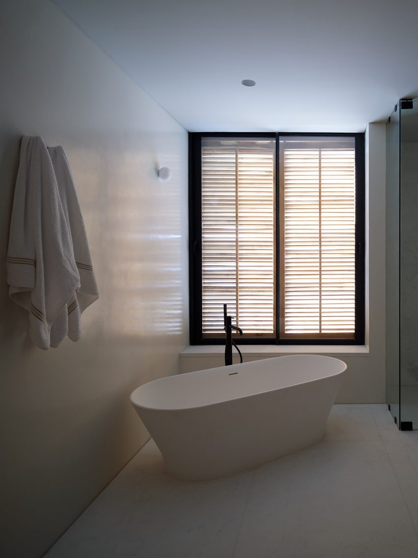 White bathroom with freestanding bathtub and window shutters