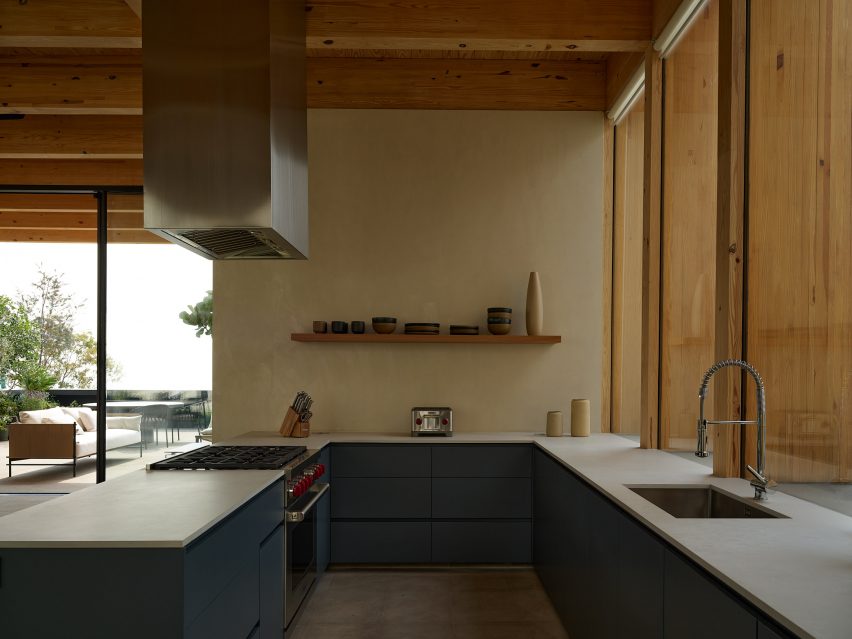 Open-plan kitchen with timber roof structure, blue kitchen cabinets, white counter tops and silver extractor fan