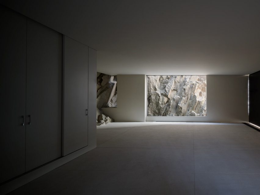 An empty, dimly lit room with a floor-to-ceiling window looking onto rocky terrain