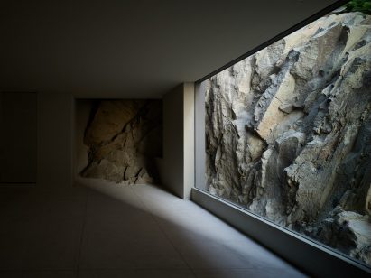 A dark empty room with floor-to-ceiling window looking onto rocky terrain