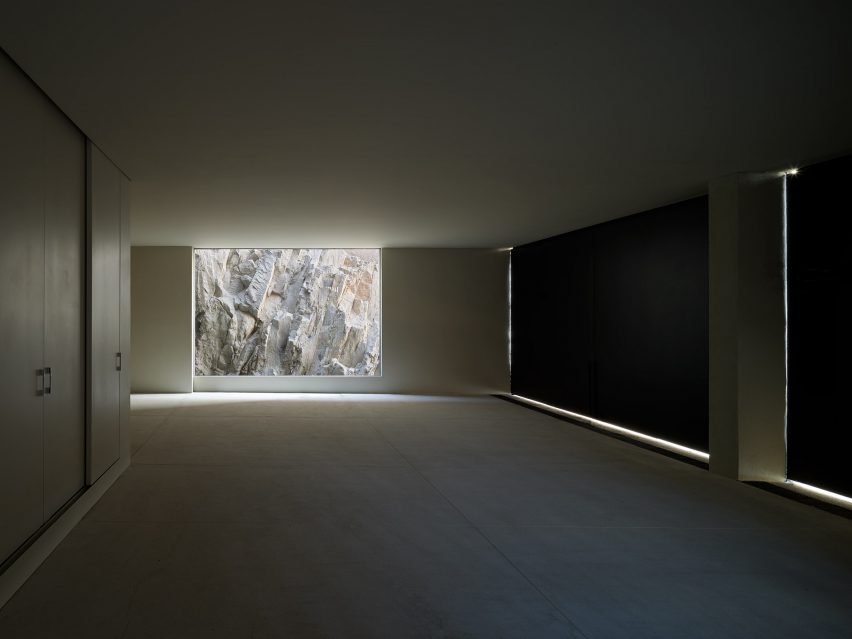 An empty, dimly lit room with a floor-to-ceiling window looking onto rocky terrain
