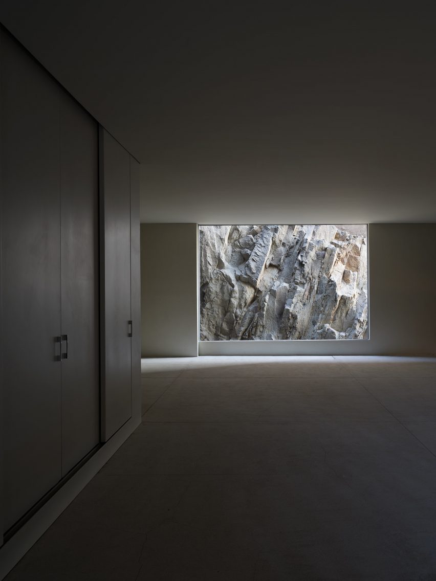 An empty, dimly lit room with a floor-to-ceiling window looking onto rocky terrain