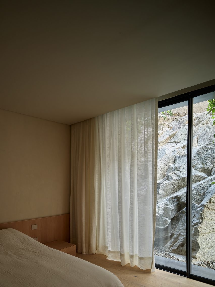 Bedroom with sheer curtains and floor-to-ceiling windows looking onto rocks