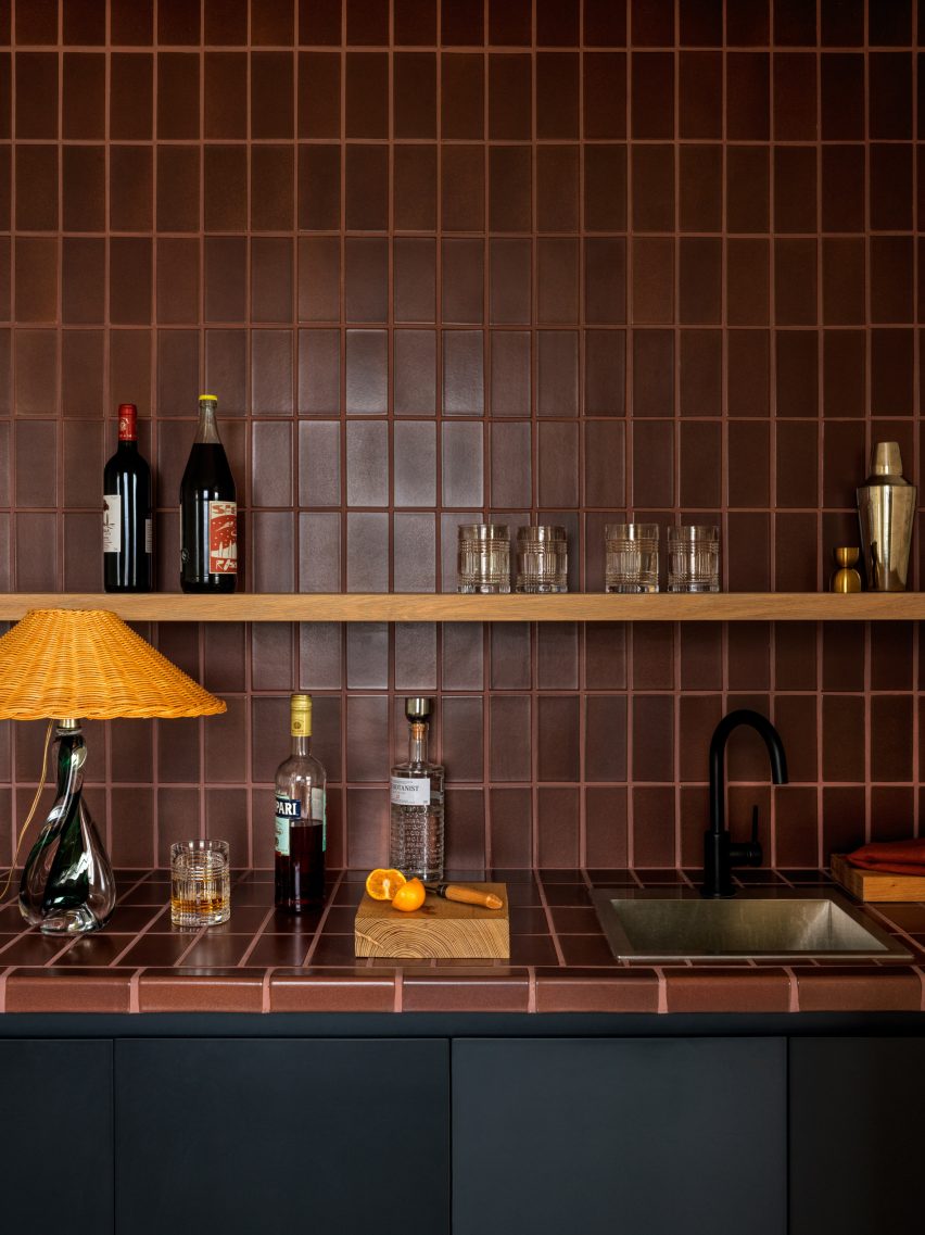 Kitchen counter and wall tiles with brown rectangle tiles, with black units and a wooden shelf