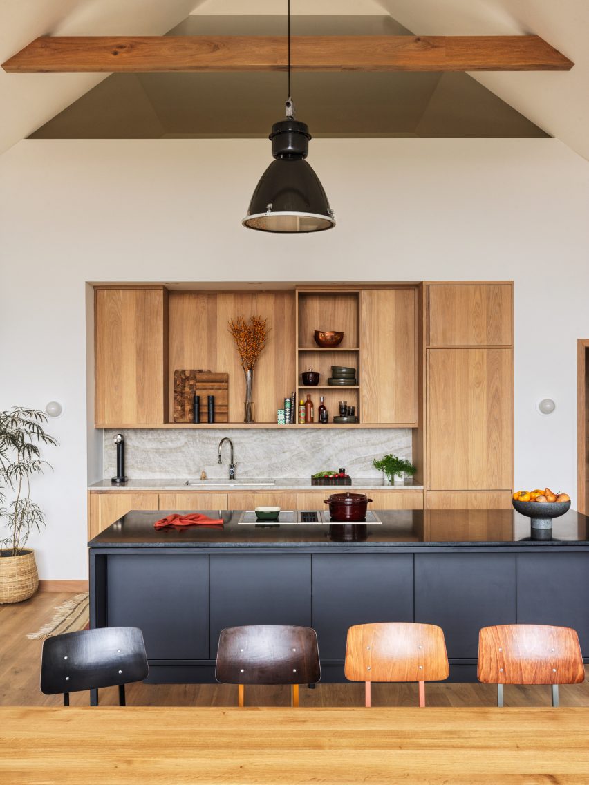 Open-plan kitchen and dining room with wooden table, black kitchen island, timber kitchen storage and exposed roof structure