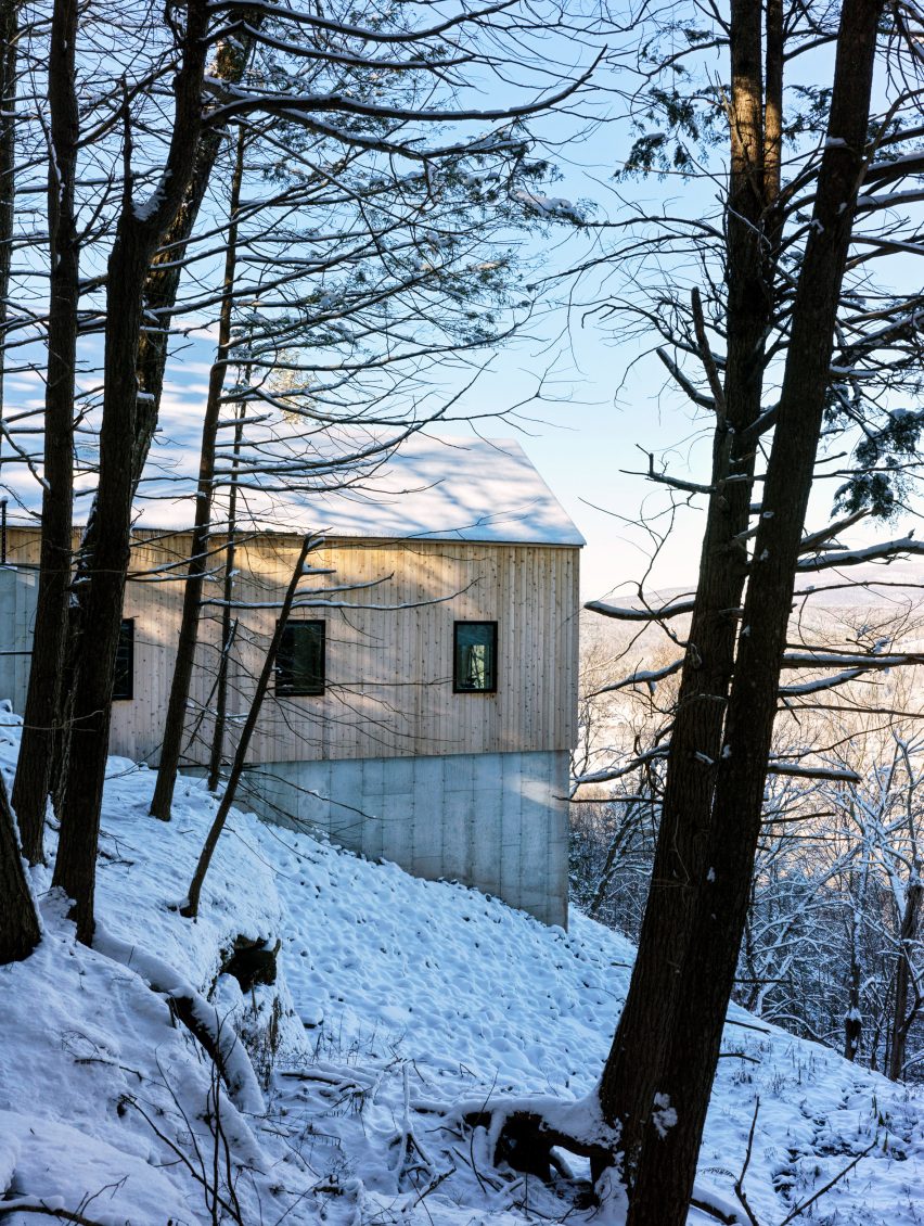 Concrete and timber-clad home on a snowy hillside in a wooded area