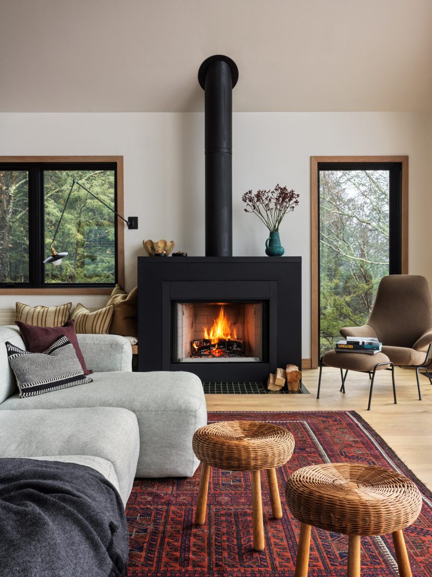 A living room with white walls, a large fireplace, patterned rug, grey sofa and woven stools