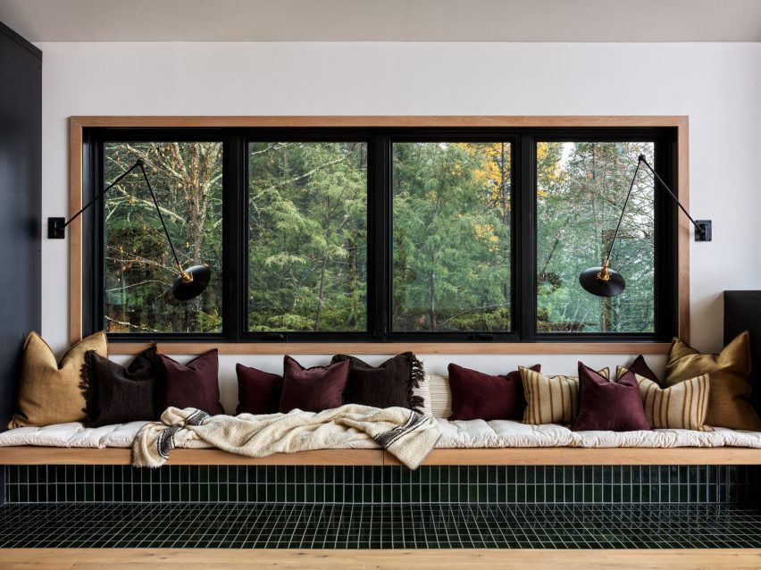 Built-in seating covered in black tiles under a window, with cream blankets and yellow and purple cushions