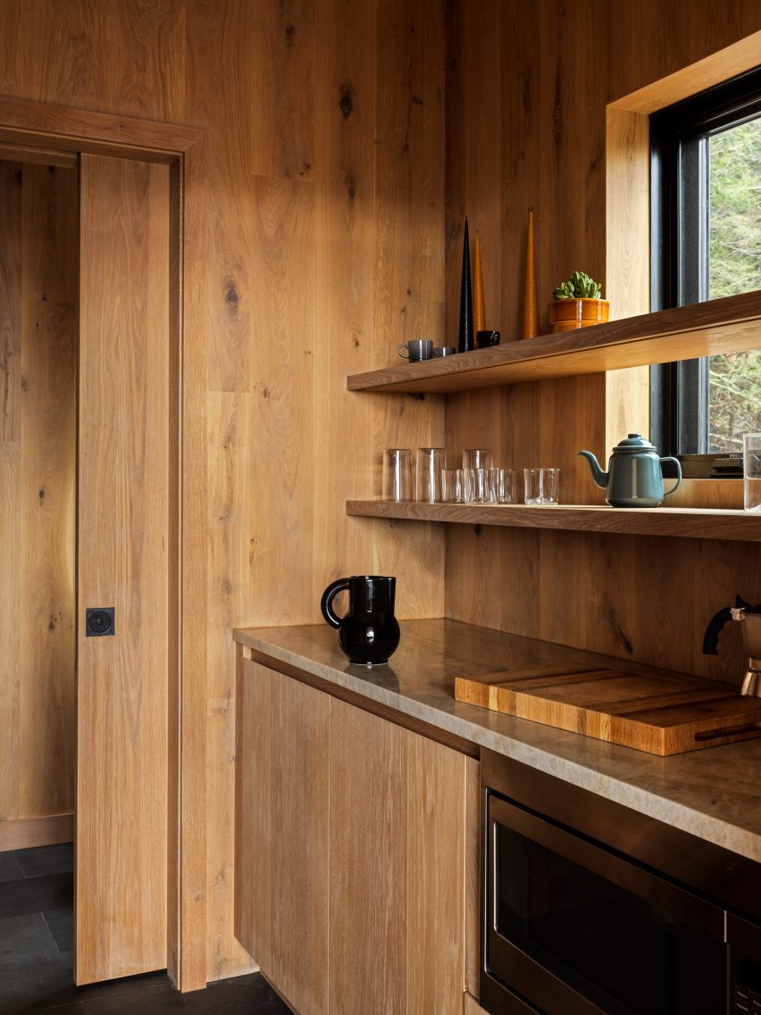 Corner of a timber-clad kitchen with a pocket sliding door, wood kitchen units and wooden shelves