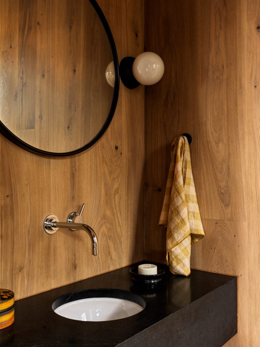 Black bathroom sink with circular wall mirror and timber walls