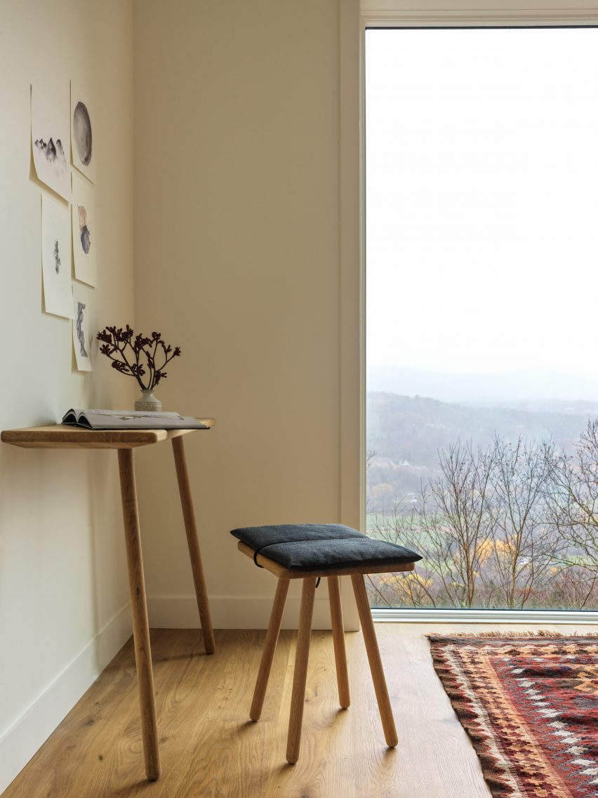 White room with wooden floors, large window and a wooden desk with a stool seat