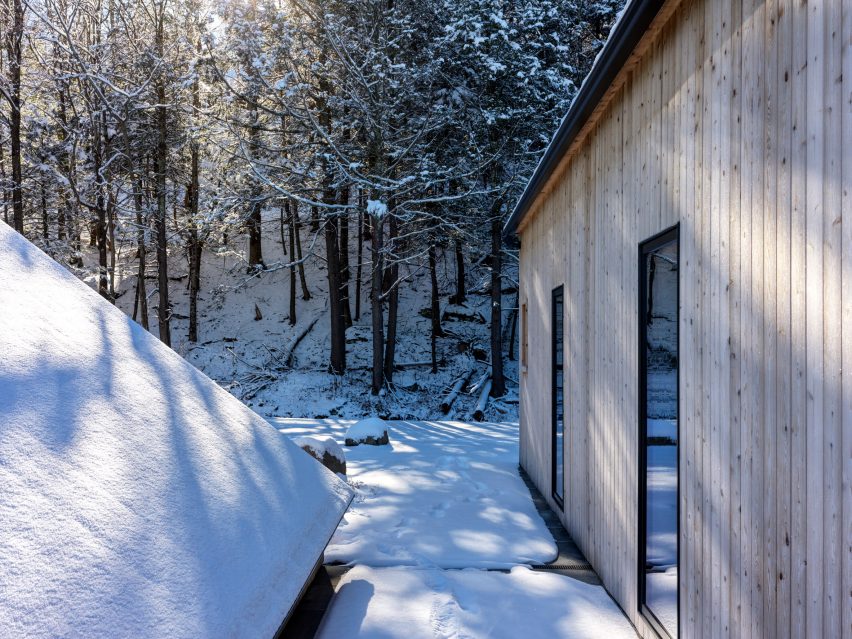 Side of a timber-clad home with tall windows in a snowy forest