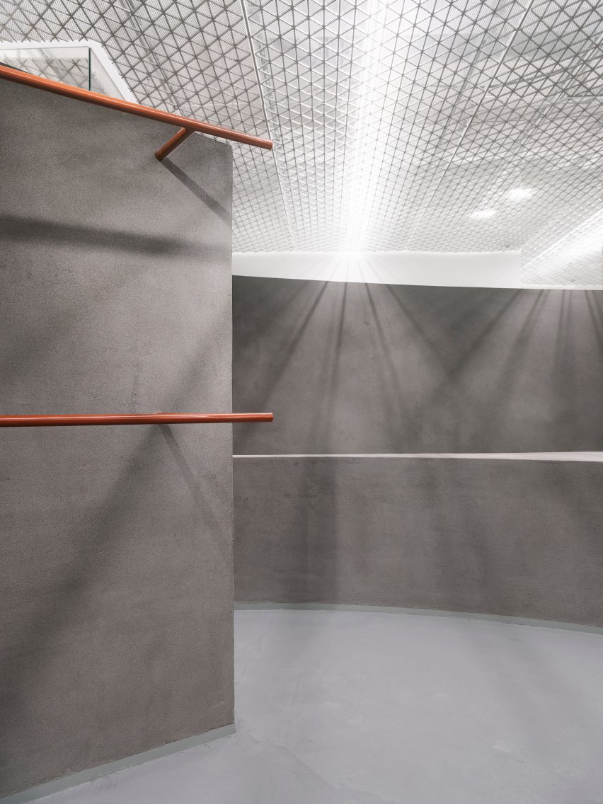 Grey shop interior with curved walls and orange clothes rails and hooks